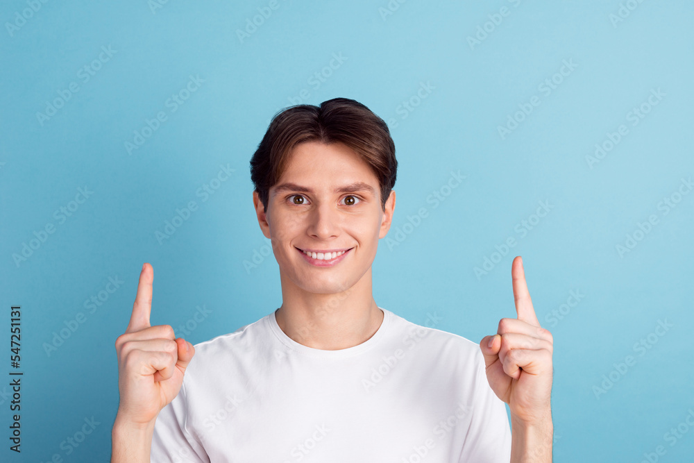 Handsome young man pointing away up looking at camera with smile while standing against blue background Handsome young man pointing away up looking at camera with smile while standing against blue background