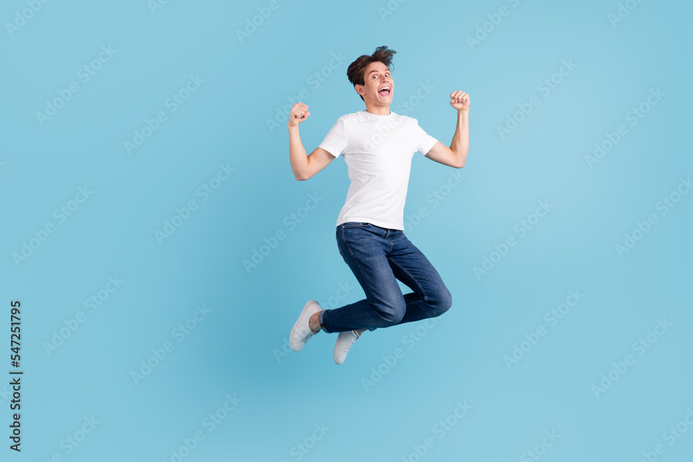 Full size photo of young happy excited smiling positive man jumping fist up victory isolated on blue color background