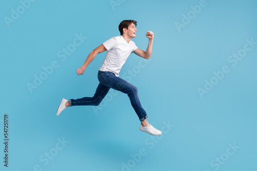 Side view of joyous man in sneakers denim outfit running in air hurrying discounts indoor studio shot isolated blue background