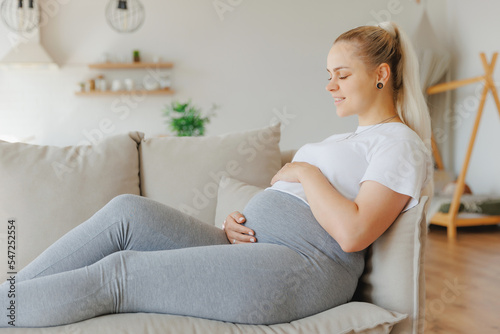 Concept pregnancy lifestyle, beauty blond scandinavian pregnant woman holding belly on gray sofa