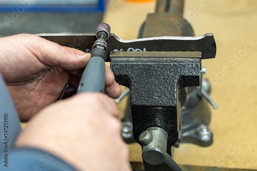 Industrial tool worker grinds a wood handle on a rotating belt sander, he makes a knife handle. photo