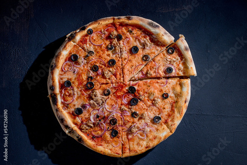 Pizza with tuna, olives, onions, mozzarella cheese and tomato sauce on a black background. Top view
