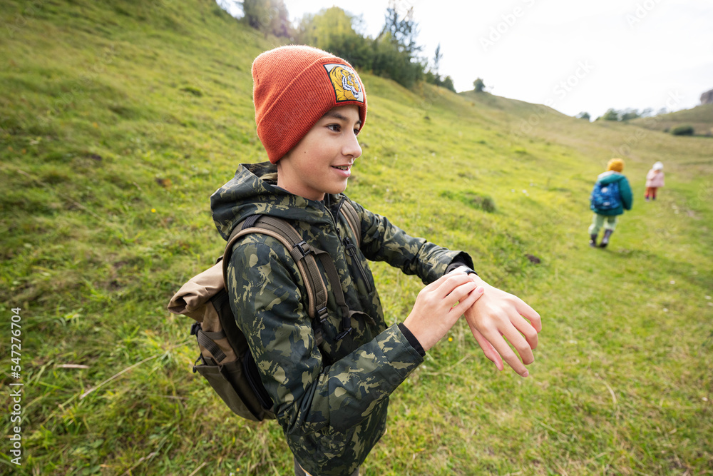 Boy with bacpack looking at his smart watches while hiking.