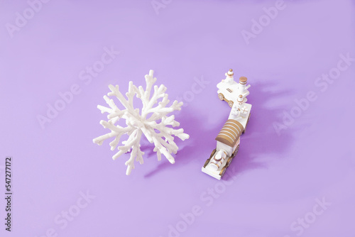 A big white snowflake and a smal train against lilac background. Top view with copy space. Minimal surreal design for winter holidays card or web banner. No one