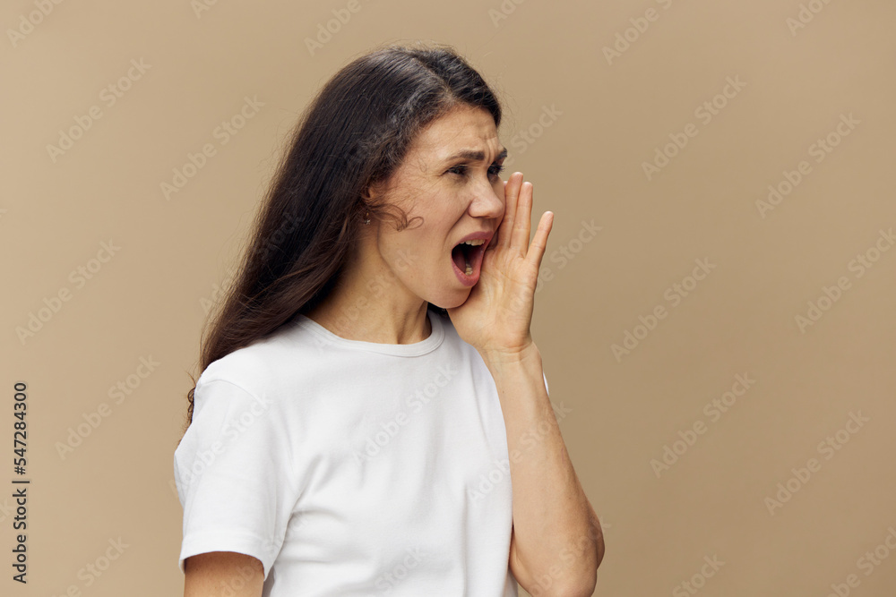 portrait of a woman in a white t-shirt standing sideways and screaming with her eyes closed standing on a beige background with empty space for an advertising mockup portrait of a woman in a white t-shirt standing sideways and screaming with her eyes closed standing on a beige background with empty space for an advertising mockup