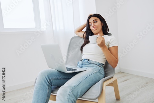 Woman relaxing at home sitting on a chair and watching a movie on her laptop with a cup of tea, autumn mood