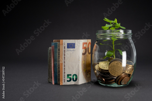 Euro banknotes on a dark background. Fifty euro banknote concept next to a glass jar with plant growing in saving coins. Copy space.