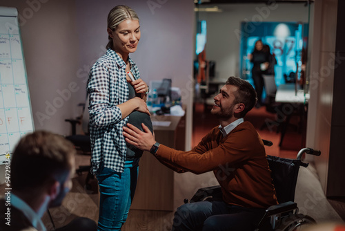 A businessman with a disability holding his pregnant wife's stomach in a modern office. 