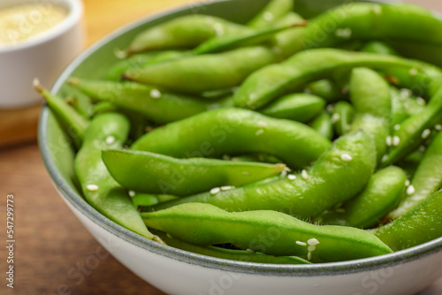 Bowl with green edamame beans in pods on wooden table, closeup