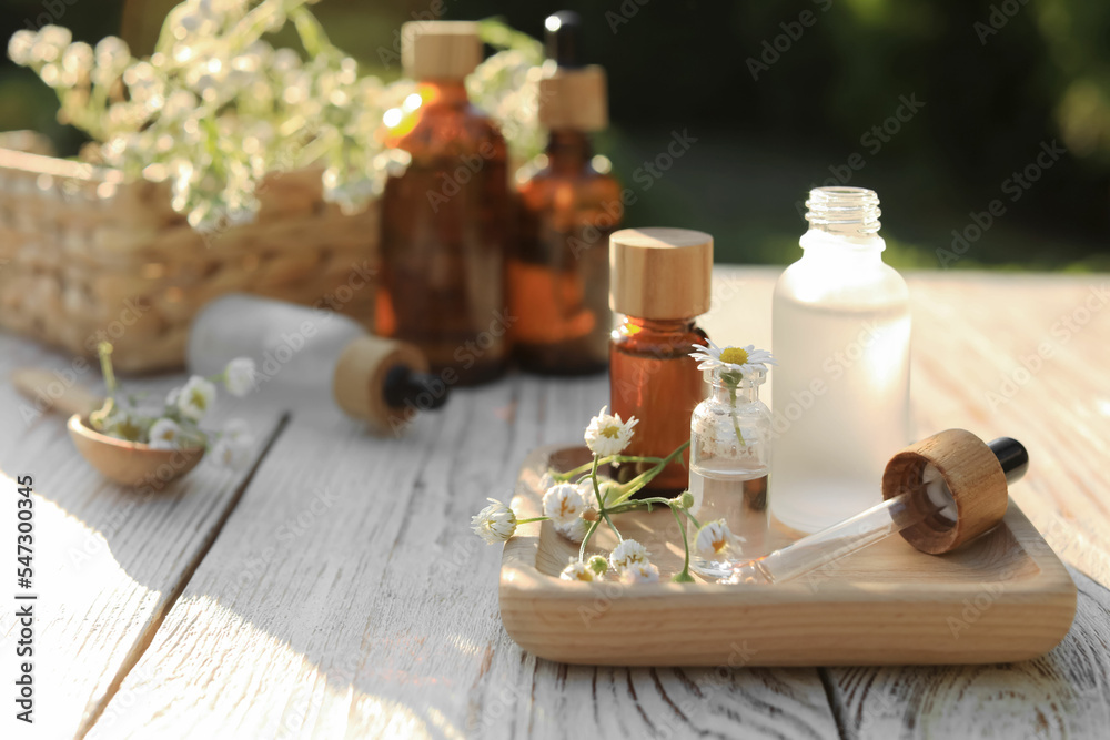 Chamomile essential oil, pipette and flowers on white wooden table outdoors, space for text Chamomile essential oil, pipette and flowers on white wooden table outdoors, space for text
