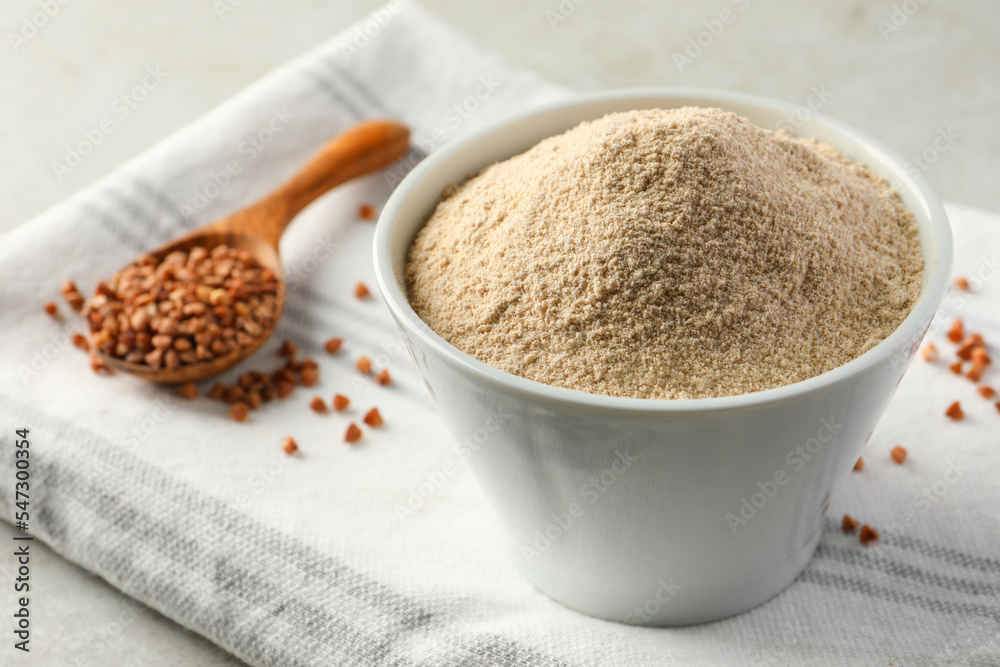 Bowl of flour and spoon with buckwheat on cloth Bowl of flour and spoon with buckwheat on cloth