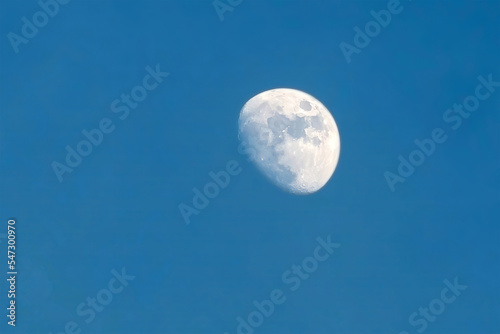 The moon rises in the daytime on the blue sky.