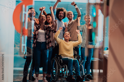 Photo of business women in wheelchairs with their hands raised in the air with their colleagues, together celebrating business success