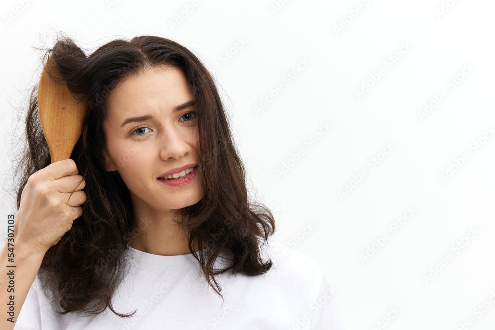 a sweet, pretty woman with long dark hair stands on a white background in a white T-shirt and holds a black comb in her hands, looking pleasantly at the camera a sweet, pretty woman with long dark hair stands on a white background in a white T-shirt and holds a black comb in her hands, looking pleasantly at the camera