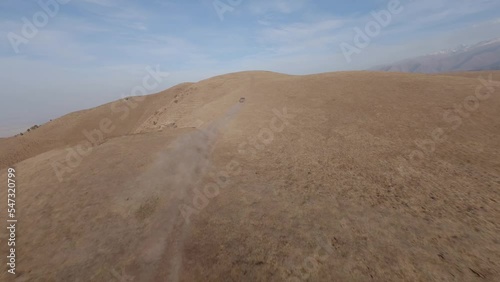 FPV sports drone follow shot SUV car drive rally offroad riding desert mountain adventure sand splash. Aerial chase view cinematic hilly valley dirt road transportation extreme tourism exploration 4k photo