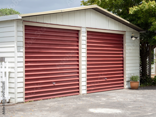 White garage with two red tilt-up retractable metal doors. © Emagnetic