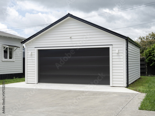 Typical double detached white garage with black tilt-up retractable raised panel metal door and gable metal roof