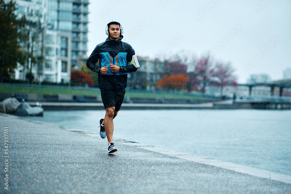 Fototapeta premium Male athlete jogging on wet path along quay during rainy day.