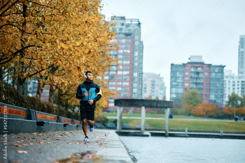 Young athletic man jogging along riverbank in rain.