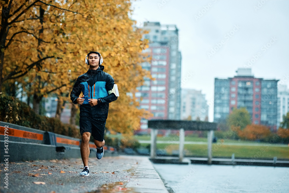 Fototapeta premium Motivated athletic man running outdoors during bad weather.