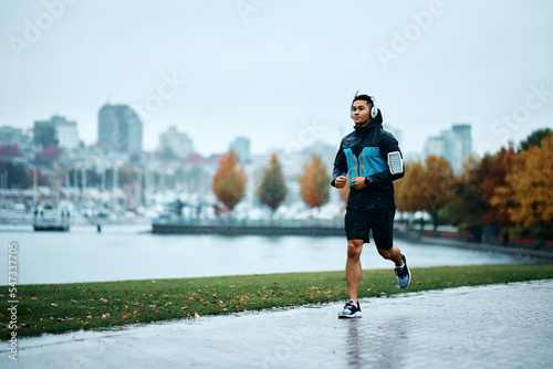 Fototapeta Athletic man jogging on quay during rainy day.
