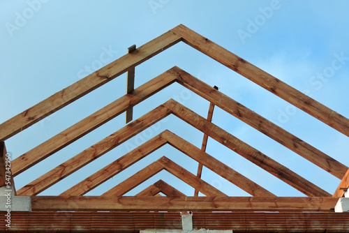 A timber roof truss in a house under construction, walls made of autoclaved aerated concrete blocks, a rough window opening, a reinforced brick lintel, blue sky in the background