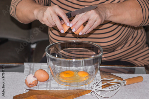 Old woman's hands cracking eggs into glass bowl with knife. Prepare for making omelet or pancakes for breakfast.