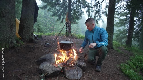 A tourist cooks food in a camp on a fire in a cauldron. A guy on a hiking trip to the mountains prepares lunch. Beautiful nature and survival in the forest. High quality 4k footage