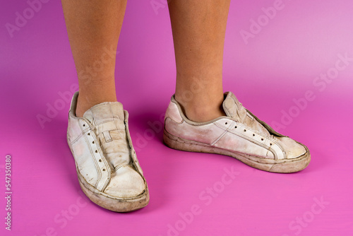 women's legs shod in old battered sneakers on a pink background