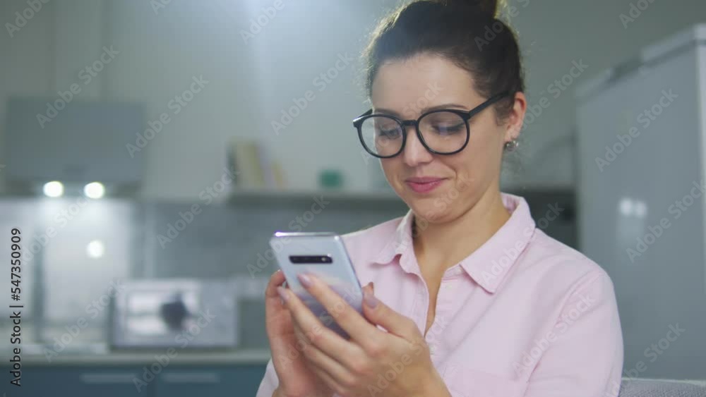 Pretty brunette woman in eyeglasses smiling, typing on mobile phone, chatting on dating app or in messengers, rejoicing, checking likes on her new photo in social networks Pretty brunette woman in eyeglasses smiling, typing on mobile phone, chatting on dating app or in messengers, rejoicing, checking likes on her new photo in social networks