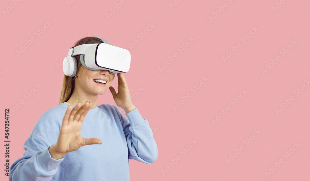 Excited teen gamer girl trying out new VR headset with sensor. Female student on solid pastel pink text space background experiences virtual reality and explores augmented world of education videogame - obrazy, fototapety, plakaty 