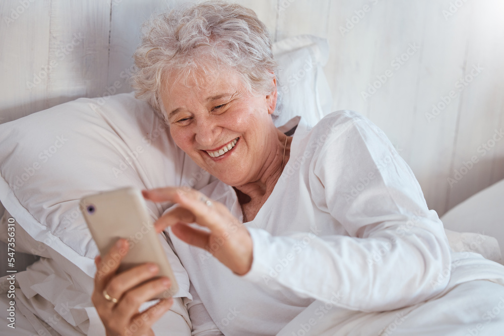 Happy elderly woman, bed or phone on social media for meme, comic or joke on internet. Senior lady, bedroom or smartphone tech with laugh at social network, funny video or email on web, app or online Happy elderly woman, bed or phone on social media for meme, comic or joke on internet. Senior lady, bedroom or smartphone tech with laugh at social network, funny video or email on web, app or online