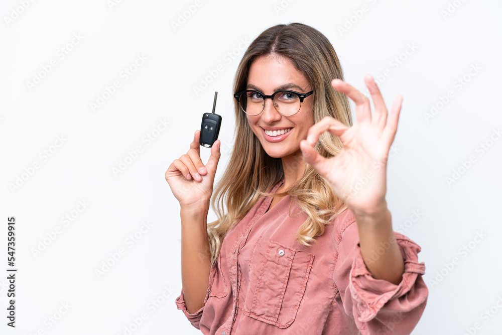 Young pretty Uruguayan woman holding car keys isolated on white background showing ok sign with fingers Young pretty Uruguayan woman holding car keys isolated on white background showing ok sign with fingers