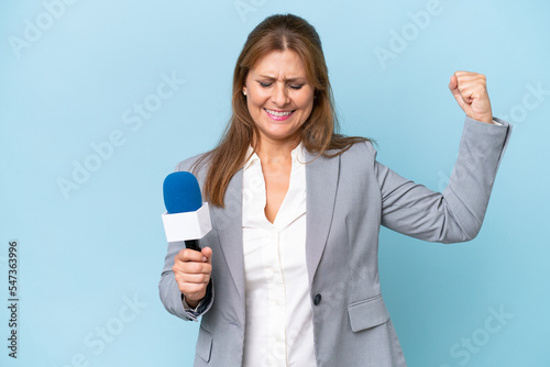 Middle-aged TV presenter woman over isolated blue background doing strong gesture