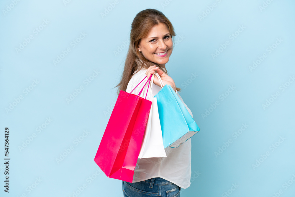 Middle-aged caucasian woman isolated on blue background holding shopping bags and smiling