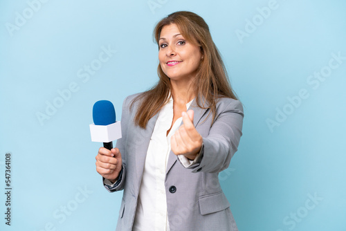Middle-aged TV presenter woman over isolated blue background making money gesture
