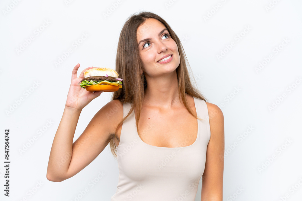 Young pretty woman holding a burger isolated on white background looking up while smiling Young pretty woman holding a burger isolated on white background looking up while smiling