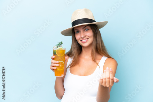 Young beautiful woman holding a cocktail isolated on blue background inviting to come with hand. Happy that you came
