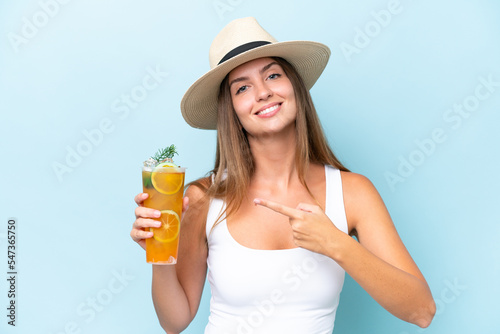 Young beautiful woman holding a cocktail isolated on blue background and pointing it