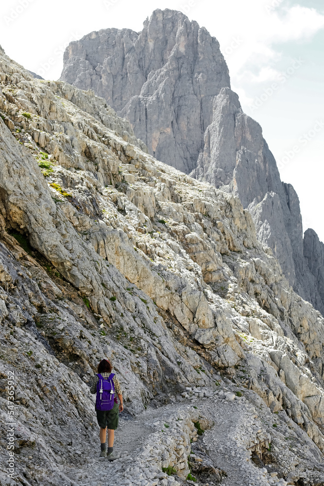 woman with backpack walks on the gravel path in the italian alps