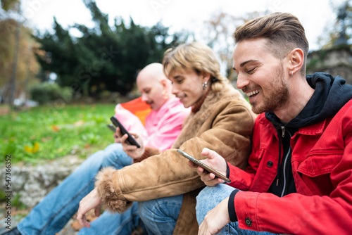 Portrait of happy young friends looking at smart phone while sitting outdoors. Caucasian people sitting at the park while using mobile phone. © Vittorio Gravino