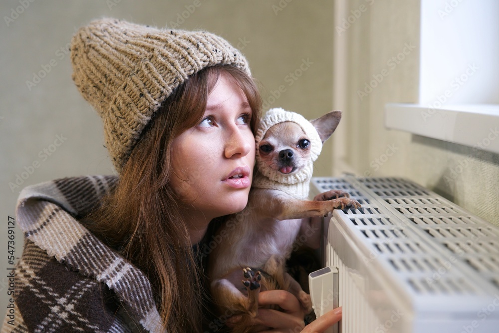 Fototapeta premium Sad cold Caucasian woman looking at the window while hugging her dog