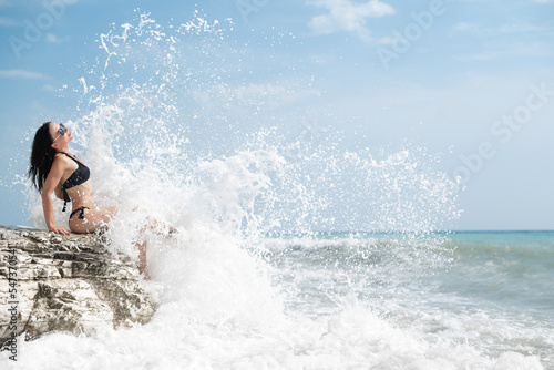 a beautiful young girl in a sexy swimsuit on a white rock by the sea in the spray from the waves