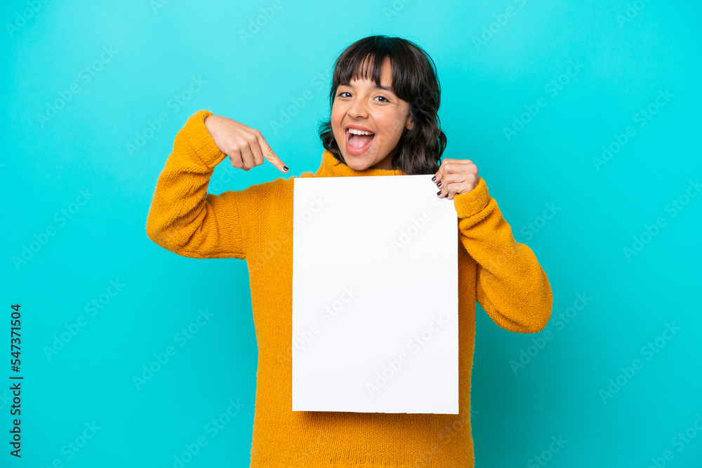 Young latin woman isolated on blue background holding an empty placard with happy expression and pointing it Young latin woman isolated on blue background holding an empty placard with happy expression and pointing it