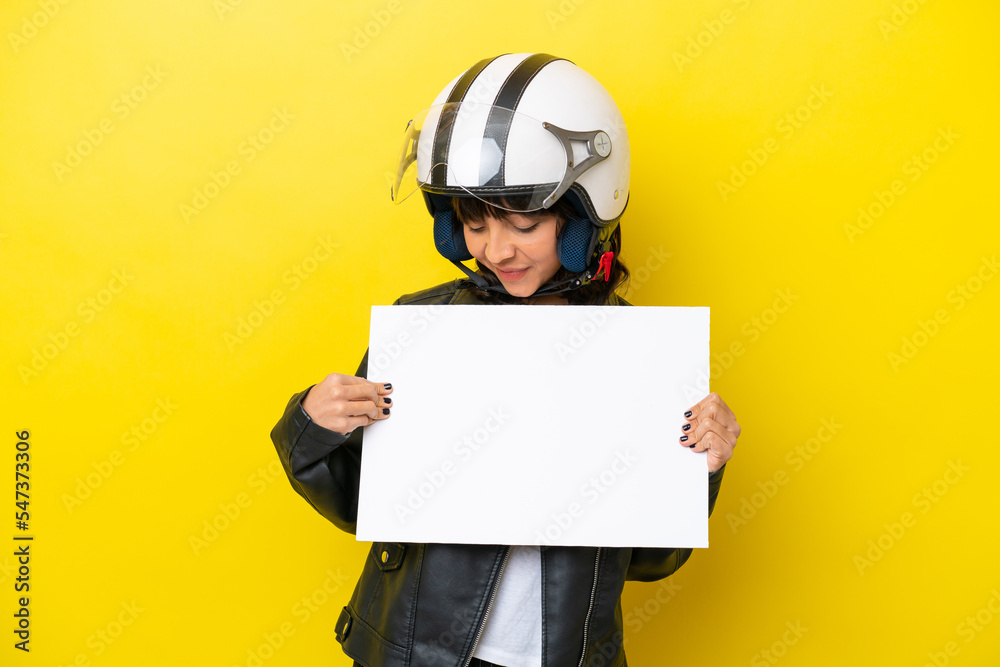 Young latin woman with a motorcycle helmet isolated on yellow background holding an empty placard with happy expression Young latin woman with a motorcycle helmet isolated on yellow background holding an empty placard with happy expression