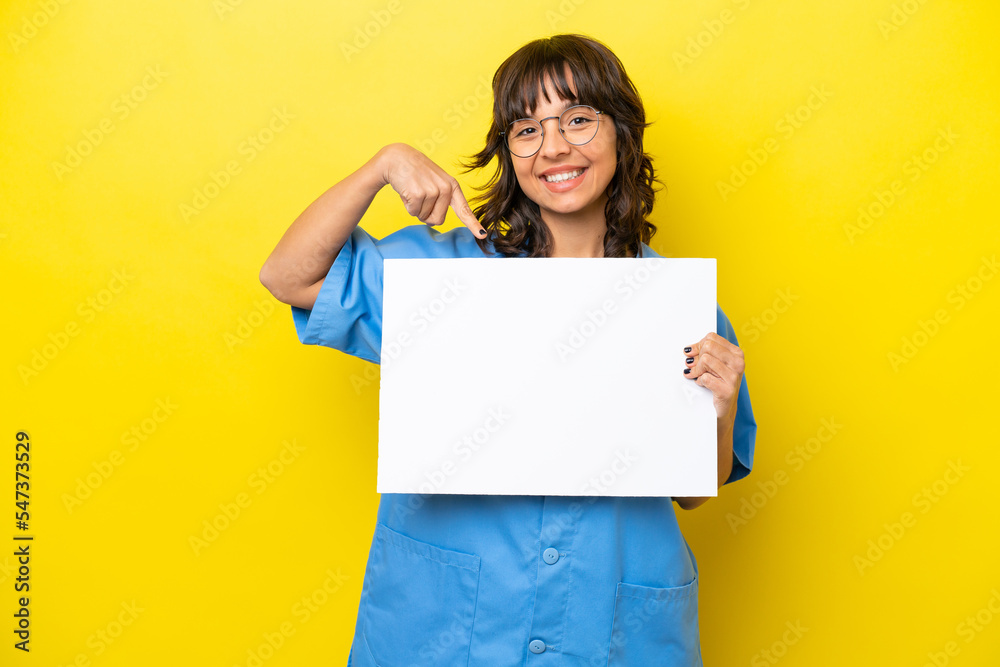 Young nurse doctor woman isolated on yellow background holding an empty placard with happy expression and pointing it Young nurse doctor woman isolated on yellow background holding an empty placard with happy expression and pointing it