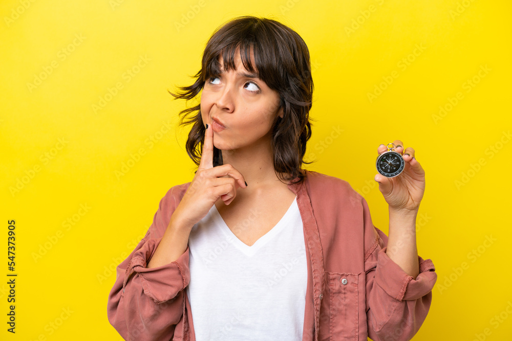 Young latin woman holding compass isolated on yellow background having doubts while looking up Young latin woman holding compass isolated on yellow background having doubts while looking up