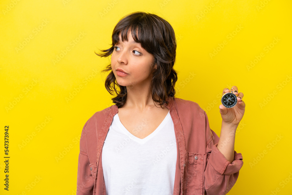 Young latin woman holding compass isolated on yellow background looking to the side Young latin woman holding compass isolated on yellow background looking to the side