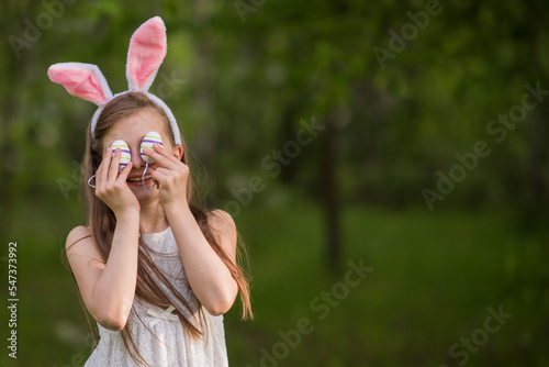Happy little girl with bunny ears and easter eggs near her face walking in the park, happy easter