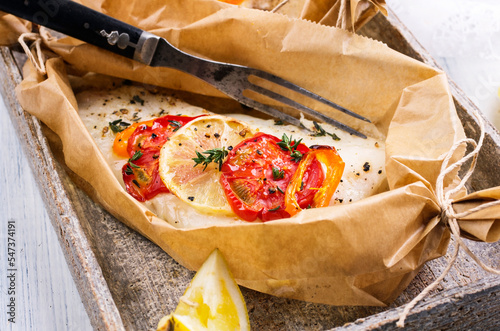 Photography Traditional baked cod fish fillet with vegetable and herbs in backing paper serv